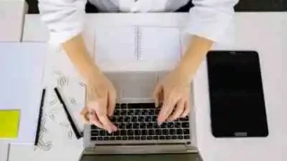 kobieta pisze na klawiaturze komputera, obok tablet i kartki papieru